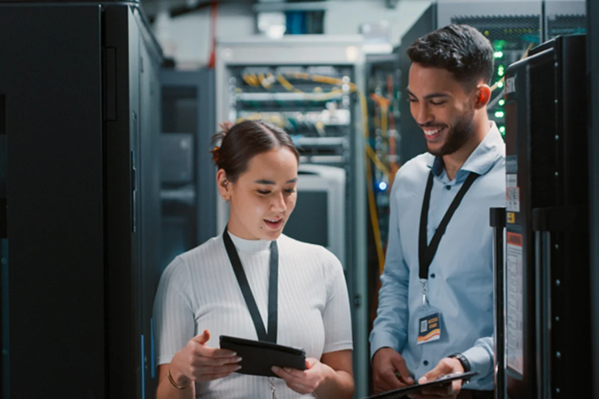 Two IT professionals reviewing a tablet while working inside a server room.