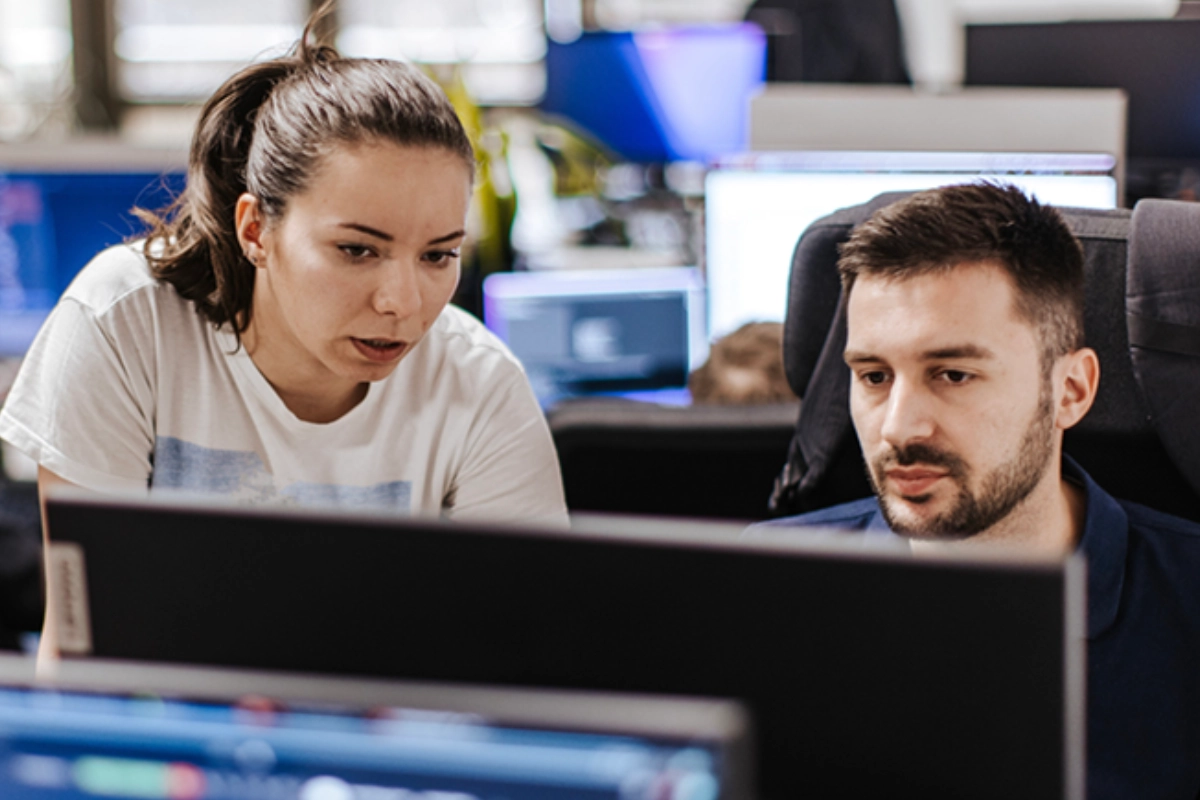 Two colleagues reviewing work together on a computer screen in a modern office.