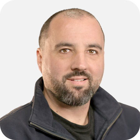 Professional headshot of a male IT support team member wearing a dark fleece against a clean white background.