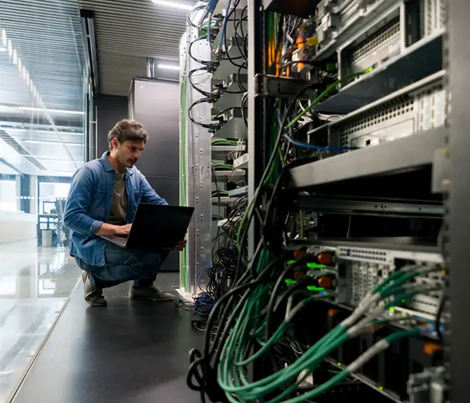 IT technician troubleshooting server racks and network cabling with a laptop
