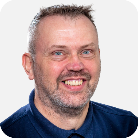 Professional headshot of a smiling male IT support team member wearing a navy polo shirt against a clean white background.